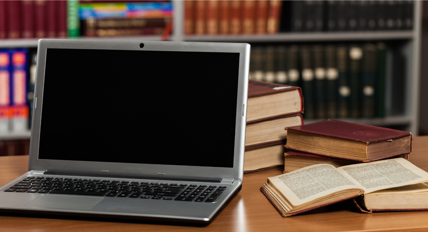 Laptop sitting on table next to open books in a library