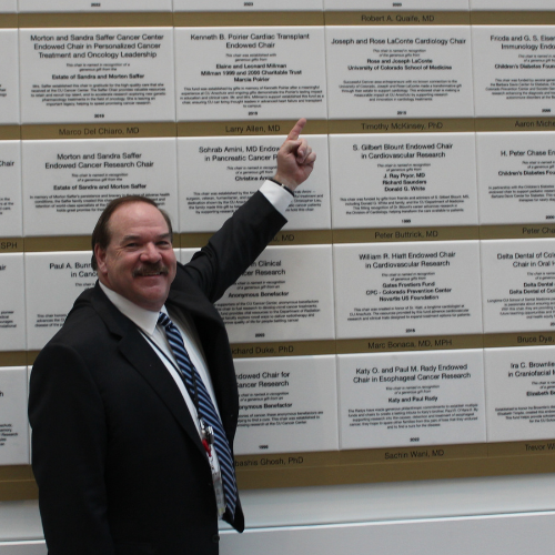 Robert Quaife, MD, points to his name and Endowed Chair plaque on the donor wall inside the Anschutz Health Sciences building.