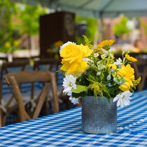 Yellow and white flower arrangement and blue gingham tablecloth decor at the 2024 Loyal Benefactor Celebration.