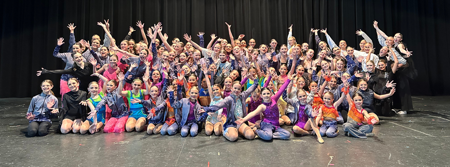 Dance for a Difference performers in costume huddle in large group and excitedly raise their arms inthe air.