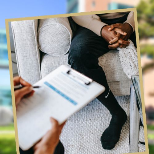 A mental health expert holds a clipboard while speaking to a patient sitting on a couch.