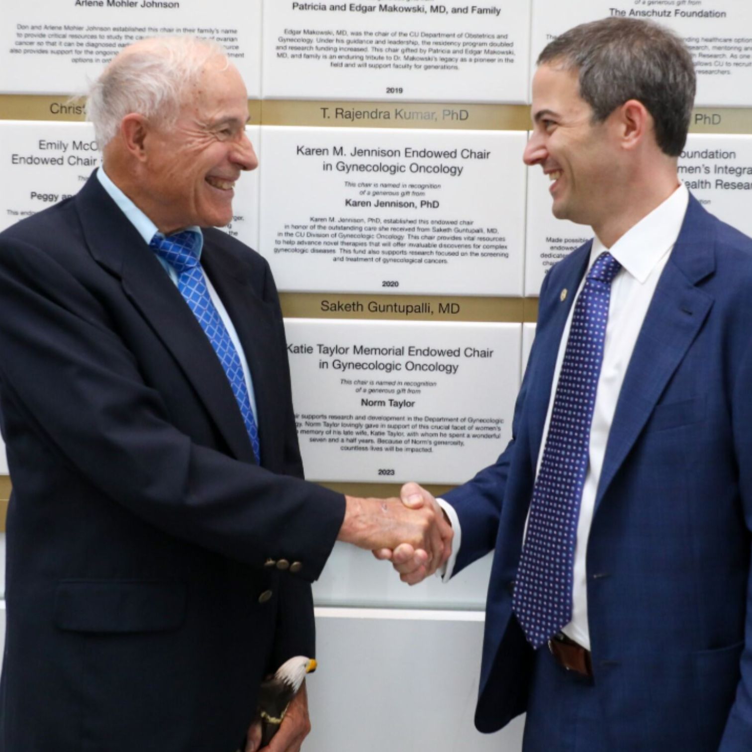 Norm Taylor and Dr. Corr shake hands in front of the Katie Taylor Memorial Endowed Chair plaque.