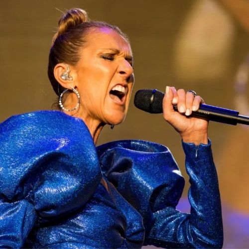 Celine Dion, wearing a sparkling blue outfit, passionately sings into a microphone.