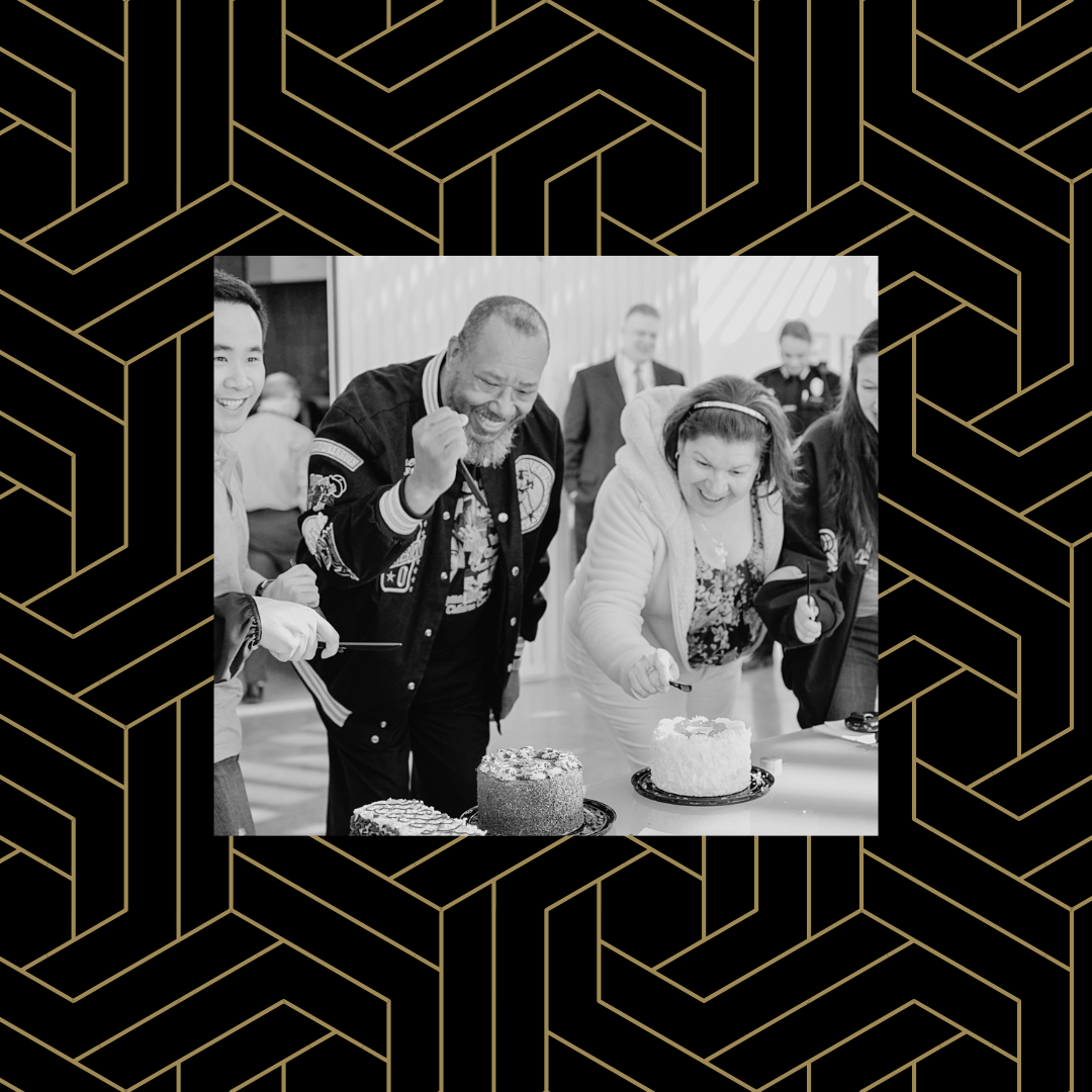 Black and white image of two community members smiling and cutting cake over a black and gold geometric background.