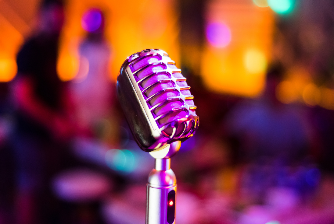 Image of a silver microphone in front of a backdrop of bright, multi-colored lights