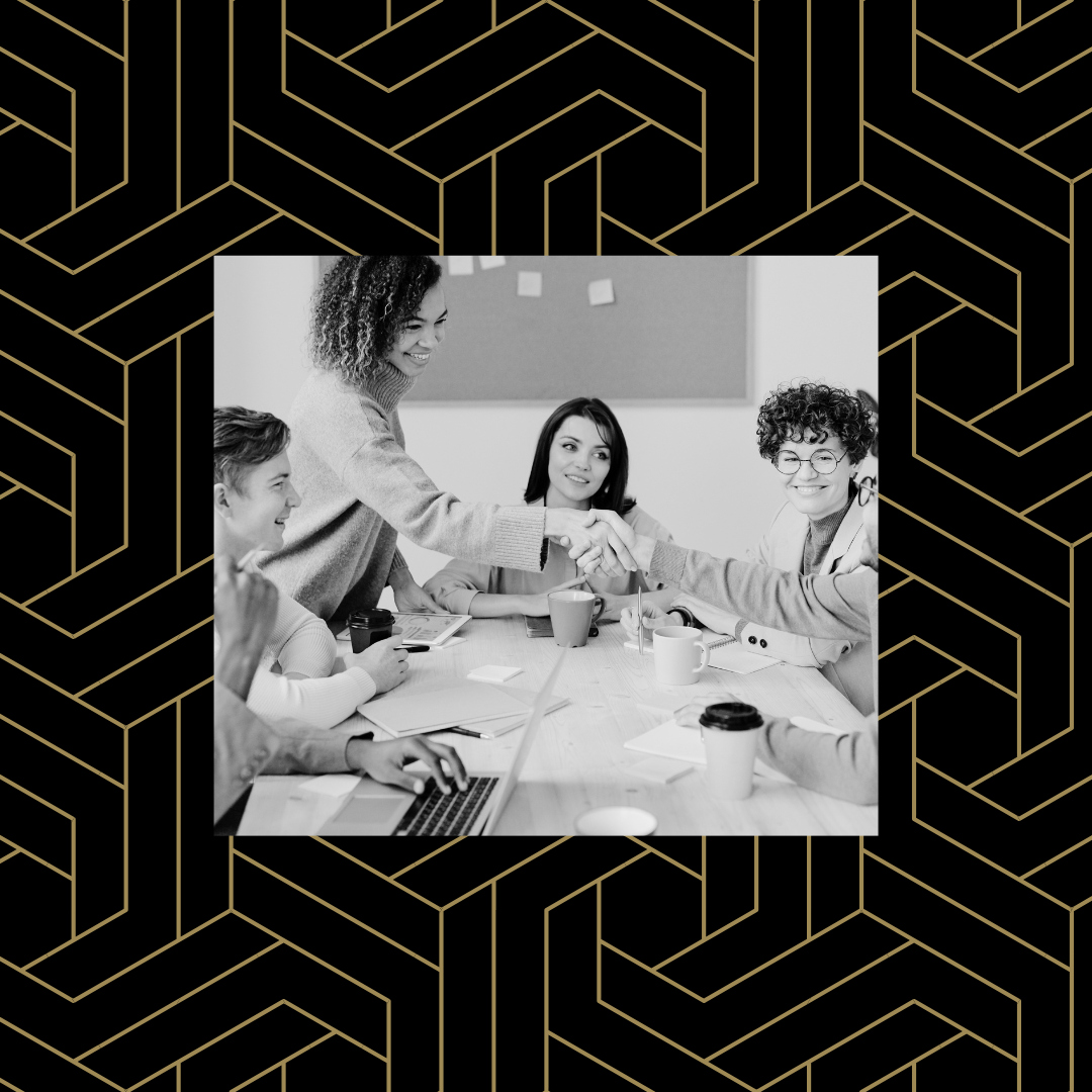 Black and white image of a group of people at a conference table with two shaking hands over a black and gold geometric pattern