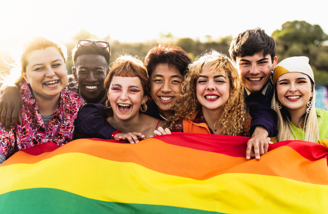 A diverse group of people hold up a Pride flag and smile