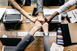 Arms and hands meeting in the middle across a table with computers